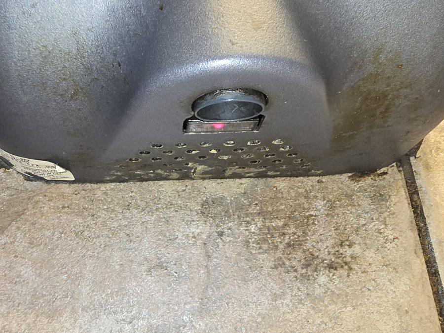 The underside of a hand dryer — grime and mold in the air vents, filth on the floor beneath